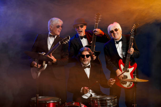 Musician group guitarist and drummer Active senior Handsome man playing guitar and drum. Best friends. Blue  background, with rays of light and special effects smoke.